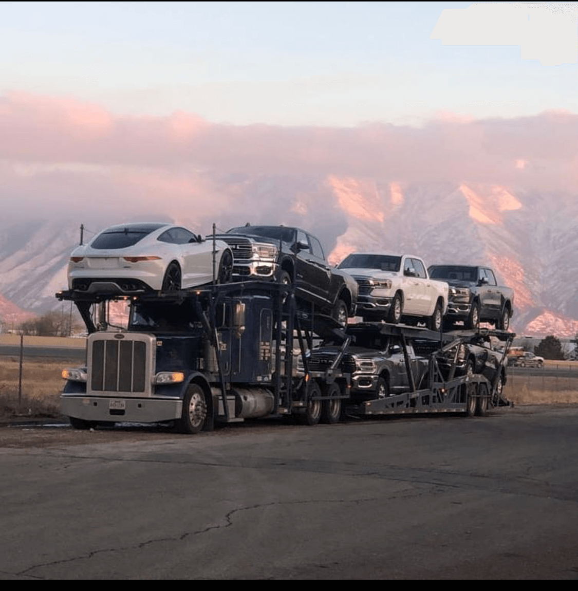 A large truck transporting multiple vehicles photographed along a scenic route.
